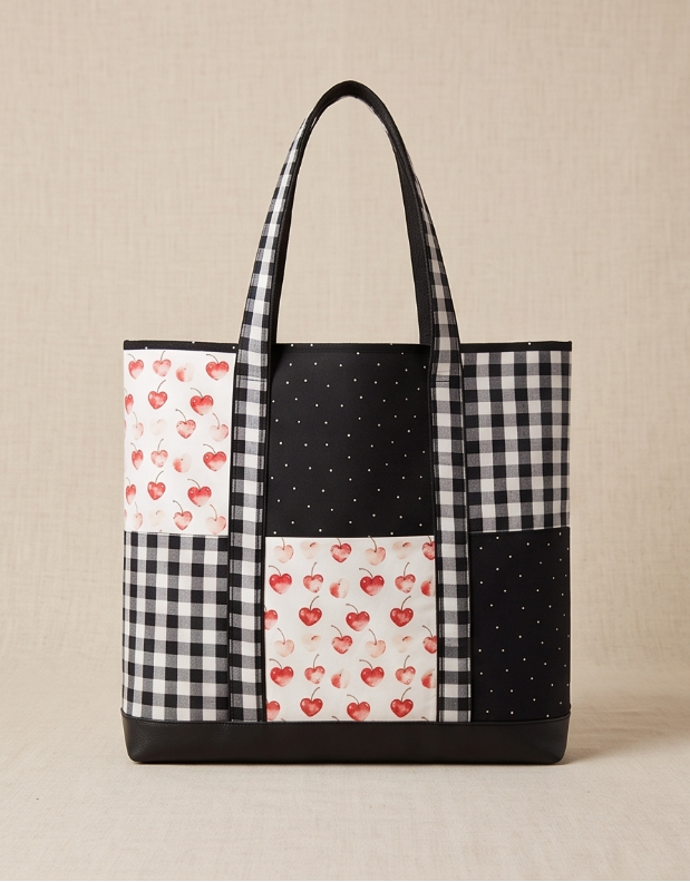 A patchwork tote bag with black and white gingham, black polka dot, and red strawberry print panels, shown on a beige background within a mobile app screenshot.